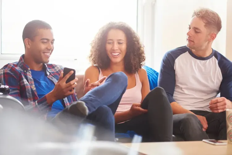 NFL survivor pool discussion among three friends on a couch as they look at a smartphone and laugh