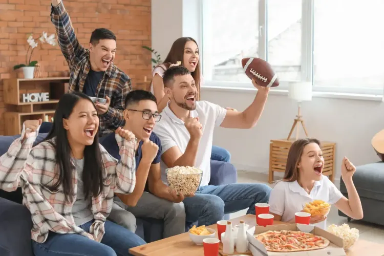Excited football fans cheering with pizza, popcorn, and snacks during a game day gathering at home