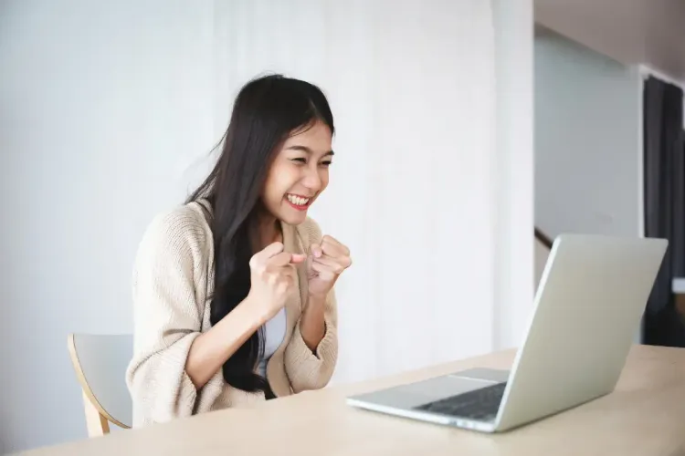 Happy woman celebrating a victory while using her laptop at home