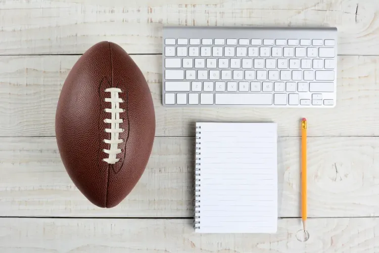 Football placed on a wooden desk next to a keyboard, notebook, and pencil.