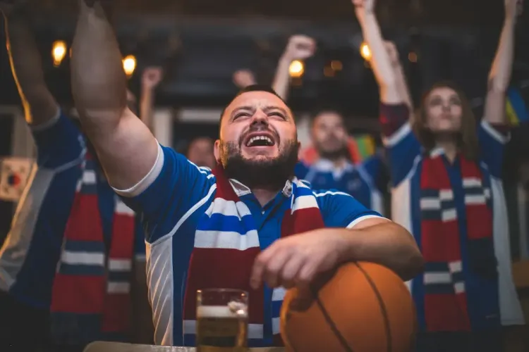 March Madness brackets excitement with passionate fans cheering in a bar, wearing team scarves and celebrating.