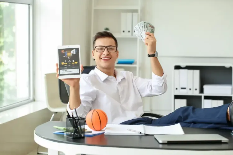 March Madness survivor pool winner celebrating with cash and a basketball game app on a tablet.