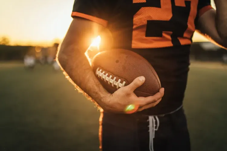Survivor pool strategy symbolized by a football player holding the ball with sunset lighting on the field.
