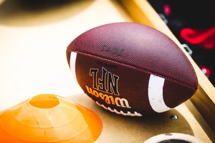 Advanced NFL stats concept shown with a close-up of a Wilson NFL football beside training cones on a bench.