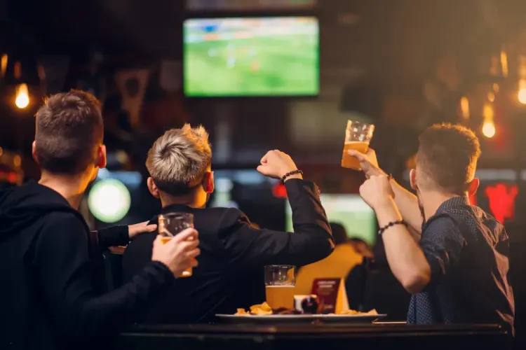 NFL knockout pool fans watching a live football match at a pub, raising beers in celebration
