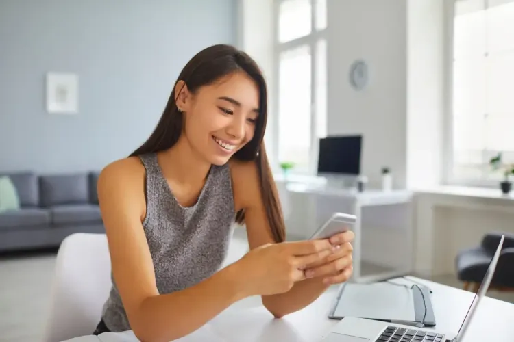 NFL betting fan smiling at phone screen while sitting at a desk with a laptop at home